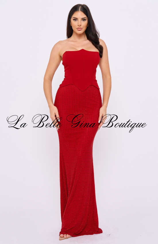 A woman wears a floor-length red mermaid gown featuring a strapless sweetheart neckline and a structured corset-style bodice. The fitted silhouette contours the body through the hips before flaring slightly at the hem. The skirt is adorned with shimmering rhinestone embellishments that add sparkle and elegance. The vibrant red color creates a bold, glamorous look perfect for formal events, galas, birthdays, and special occasions.